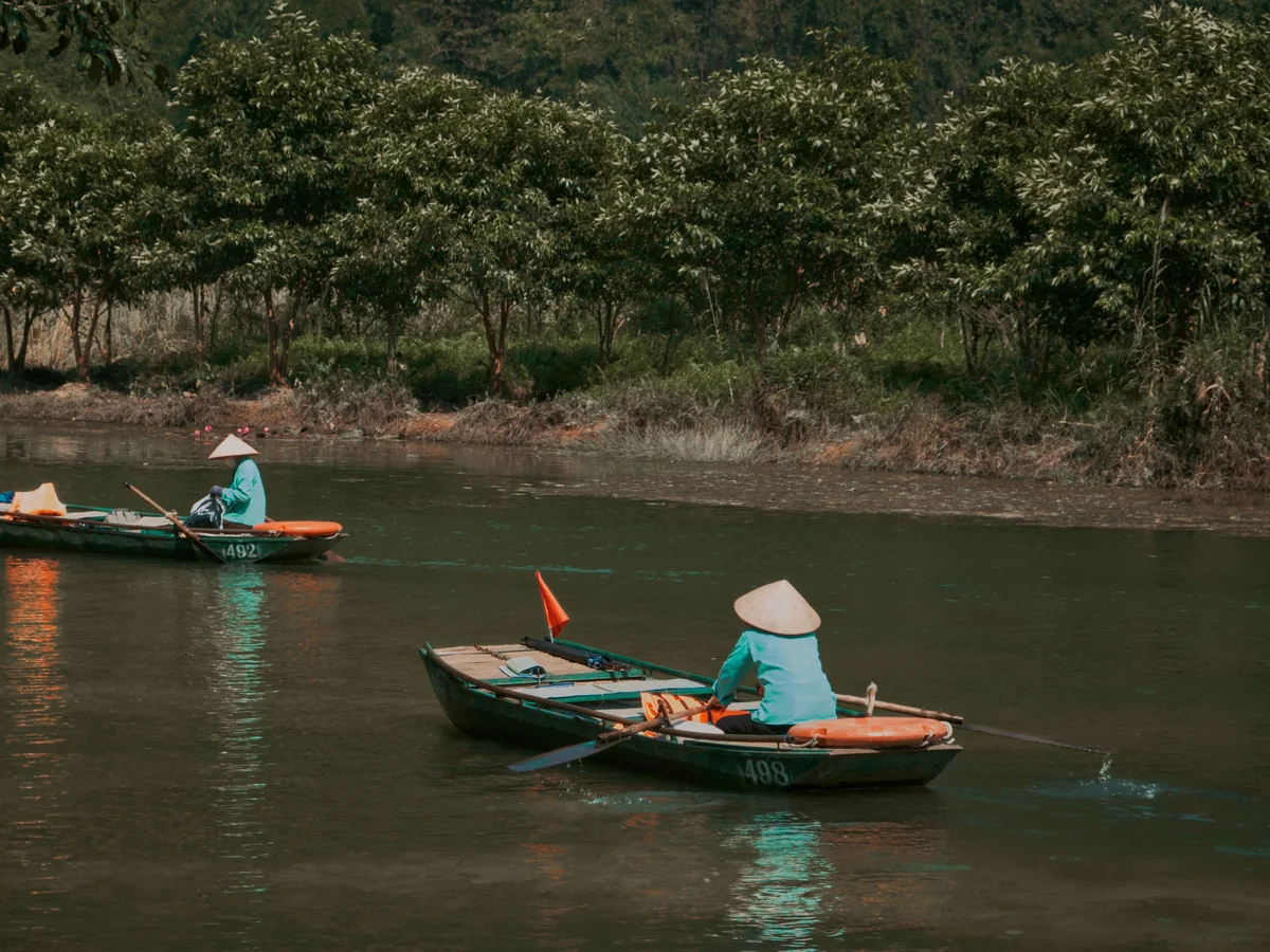 Two hand-rowed boats with nón lá-wearing rowers on a Vietnamese river, representative of the delta's sampan travel